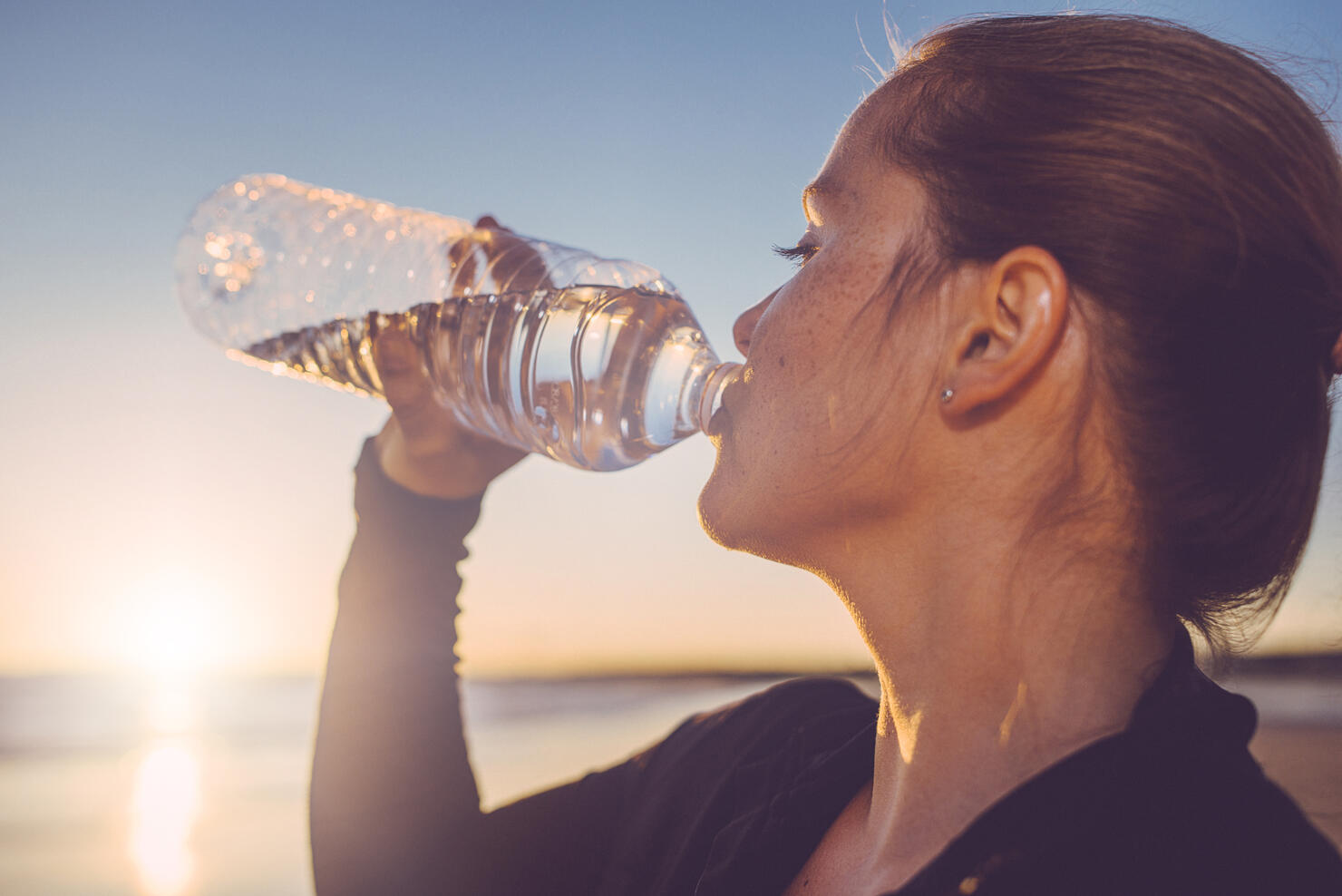 Woman drinking water seaside.