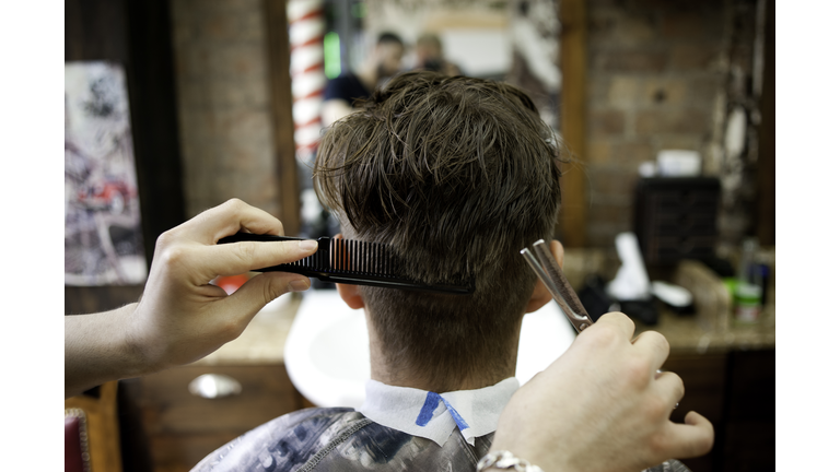 Rear view of young man in barbershop having haircut