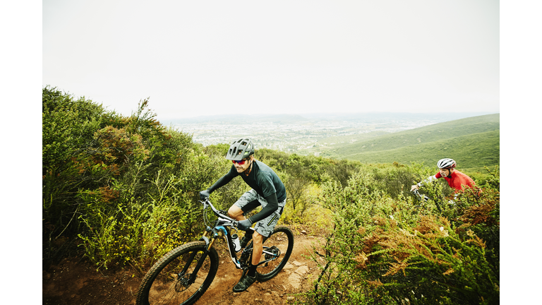 Mature man climbing up trail during early morning mountain bike ride with friend