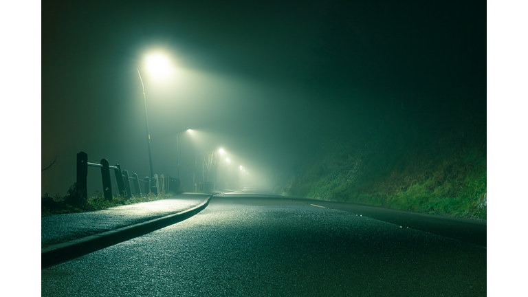 Low angle of a spooky country road, going into the distance with street lights, glowing on a moody foggy winters night