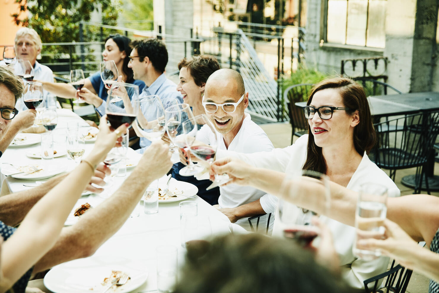 Laughing friends toasting during celebration dinner on restaurant patio on summer evening