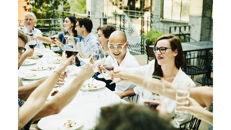 Laughing friends toasting during celebration dinner on restaurant patio on summer evening