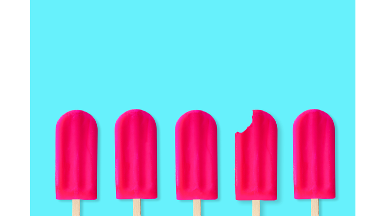 Pink popsciles on a pastel blue background. One with bite removed.