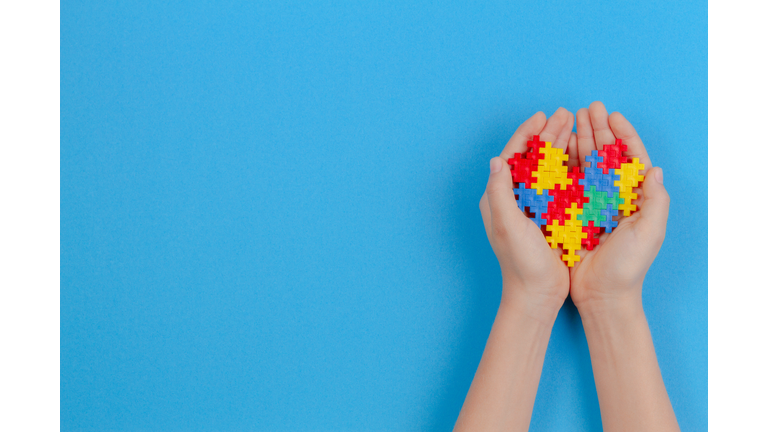 Kid Hand Holding Colorful Heart On Blue Background. World Autism Awareness Day Concept.