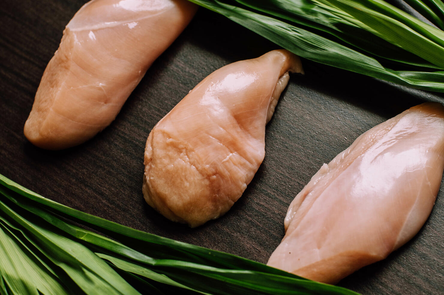Raw chicken breast fillets and pandan leaves on a wooden table