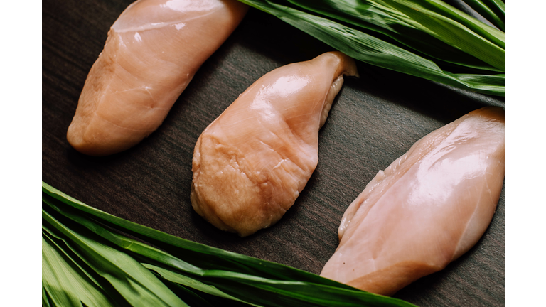 Raw chicken breast fillets and pandan leaves on a wooden table