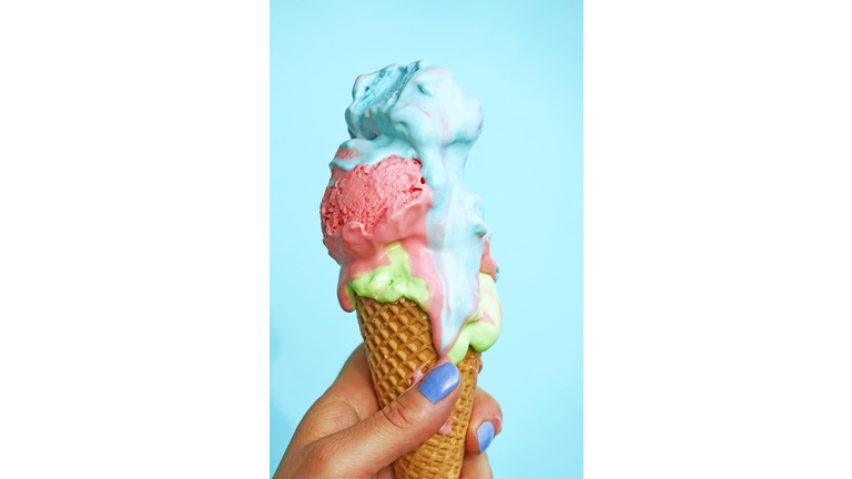 Woman's hand holding ice-cream cone with melting icecream in front of blue background