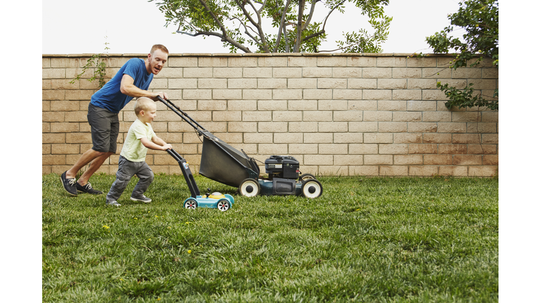Father and son mowing lawn in backyard