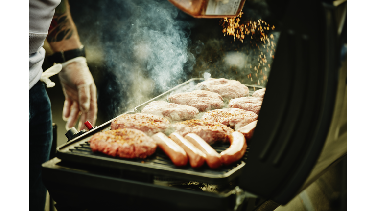 Man seasoning burgers and hot dogs on barbecue