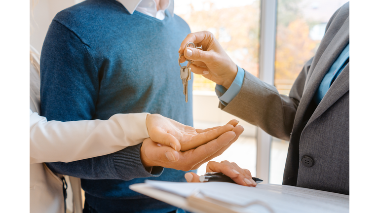 Midsection Of Agent Giving House Key To Customers In Office