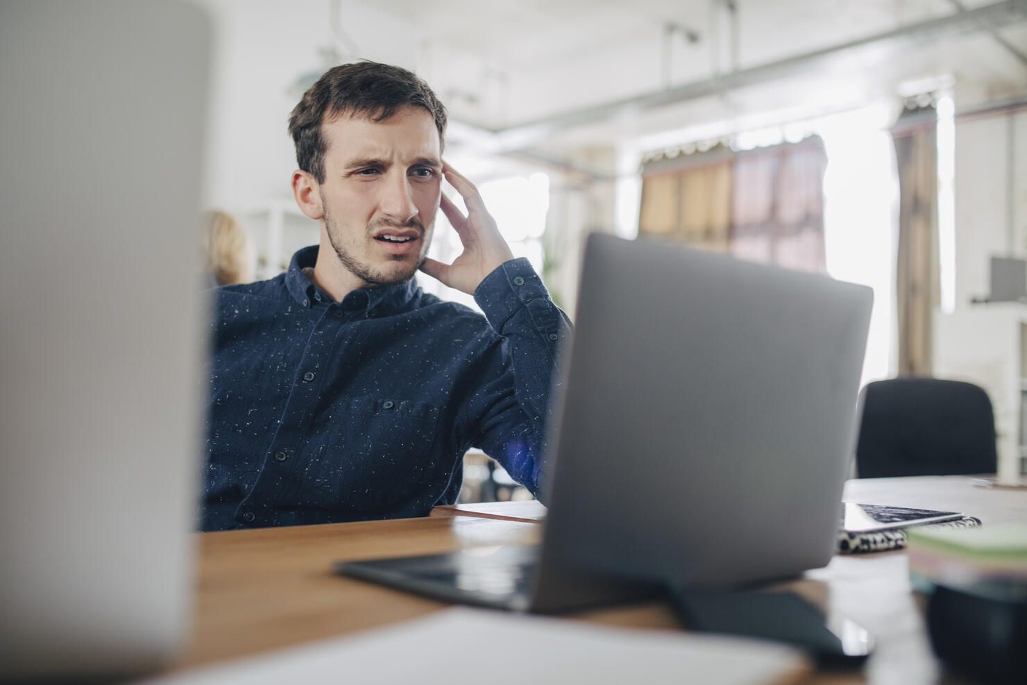 Confused businessman looking at laptop while sitting at desk in office