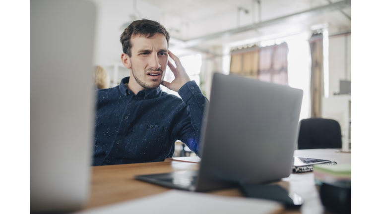 Confused businessman looking at laptop while sitting at desk in office