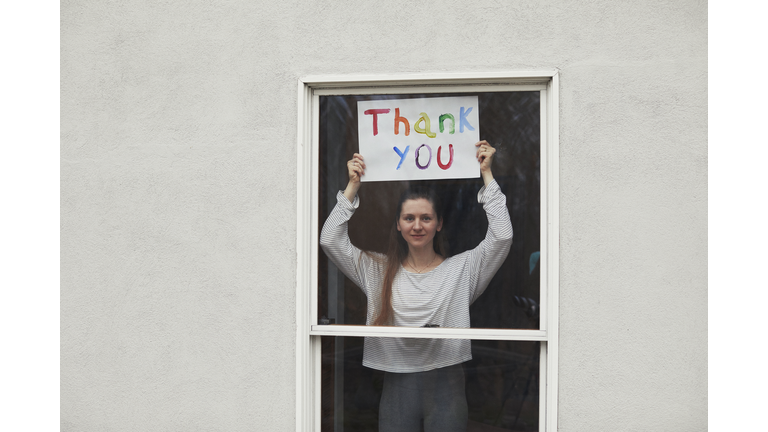 Young women holding up Thank You sign in window looking out