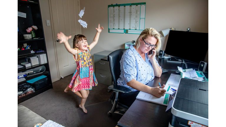 Middle Aged Women working from home in office whilst also looking after her young daugther.