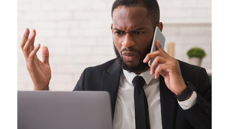 Furious black businessman scolding assistant by phone