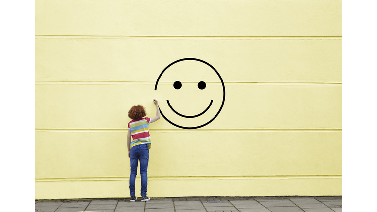 Girl drawing smiley face on to a wall