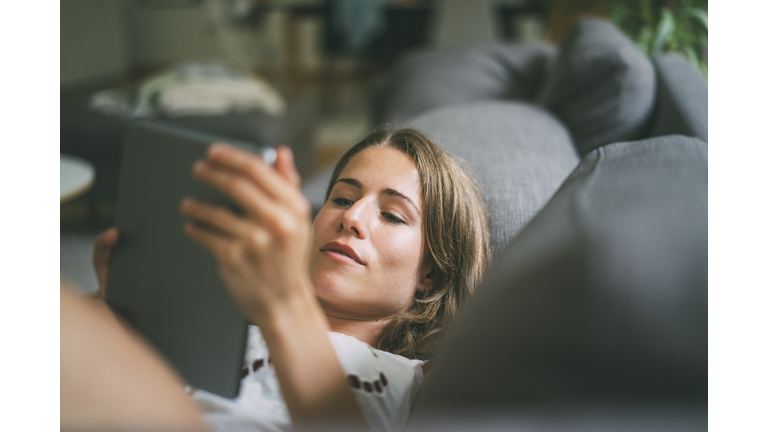 Relaxed young woman lying on couch using tablet