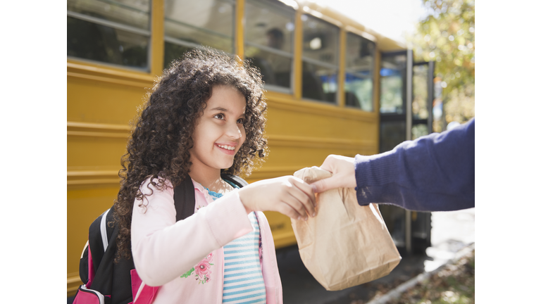 Mother handing daughter sack lunch