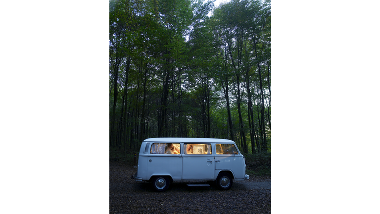 "Family in illuminated van in forest, side view, evening"