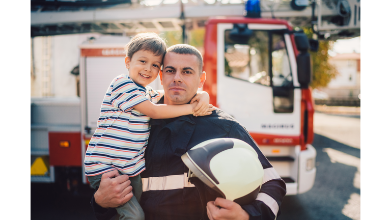 Portrait of firefighter holding little boy on hands