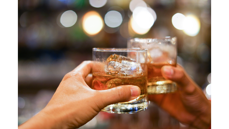 two men clinking glasses of whiskey drink alcohol beverage together at counter in the pub