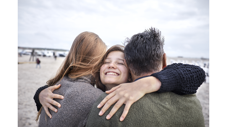 Happy girl hugging woman and man on the beach