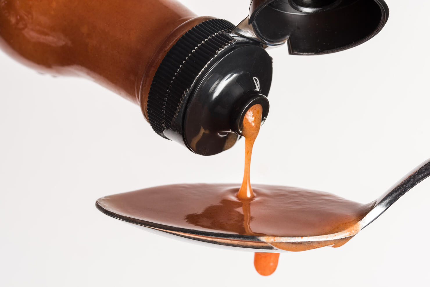 Close-Up Of Bottle Pouring Hot Sauce In Spoon Against White Background