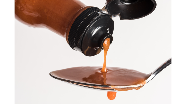 Close-Up Of Bottle Pouring Hot Sauce In Spoon Against White Background