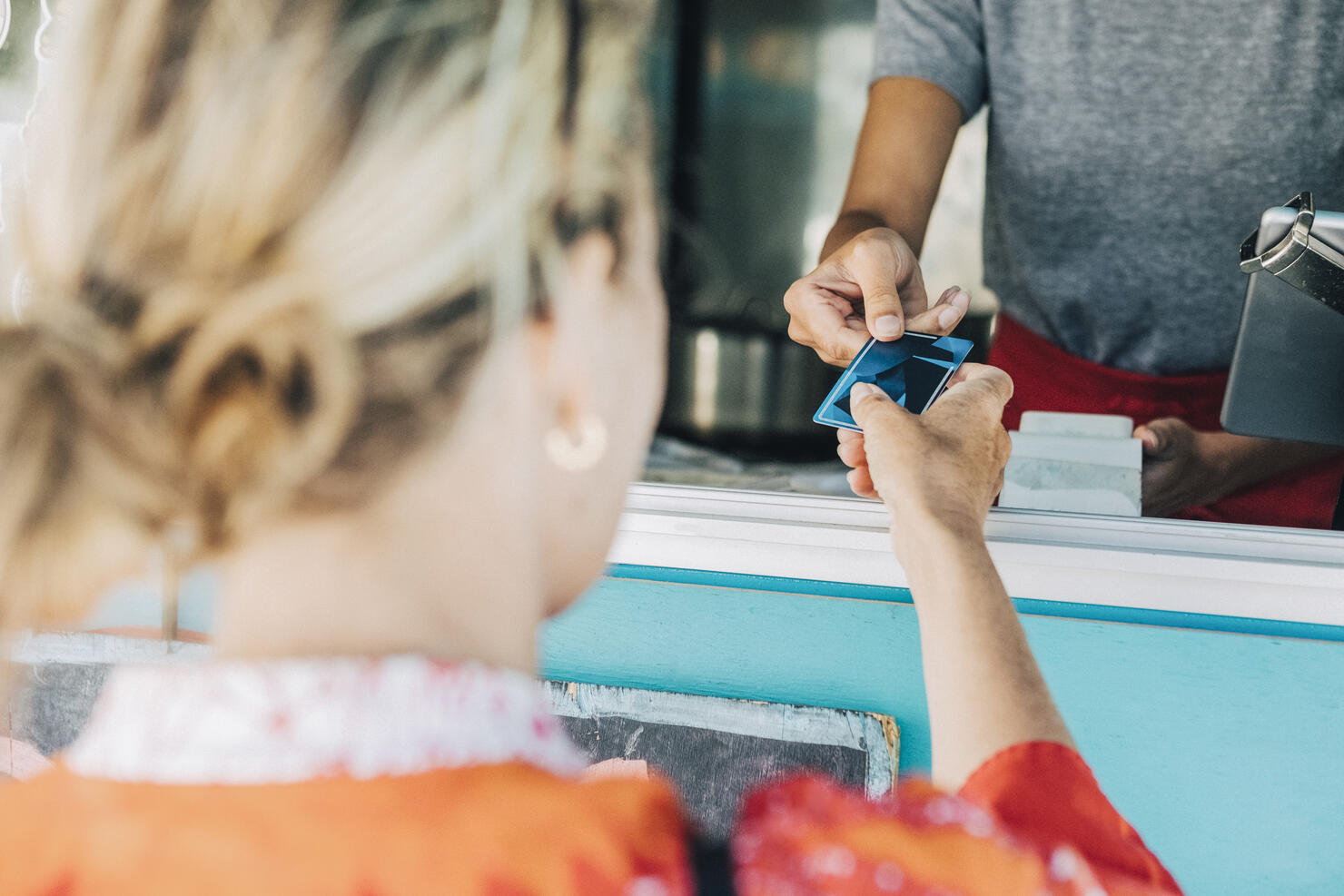 Rear view of female customer giving credit card to owner standing in food truck