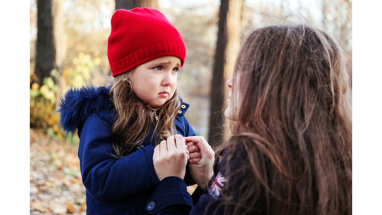 Scared daughter holding mother's hands in autumn park. Child girl express sad emotions, complain about their own problems