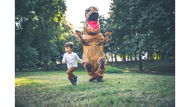 Person Wearing Dinosaur Costume Chasing Boy In Park