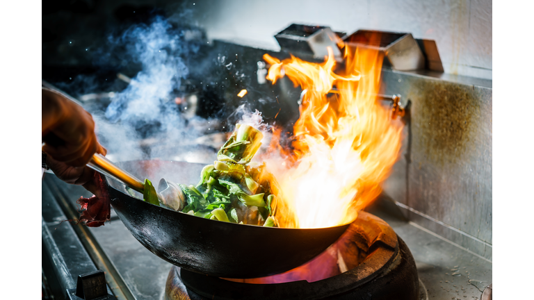 Chef in restaurant kitchen at stove with high burning flames