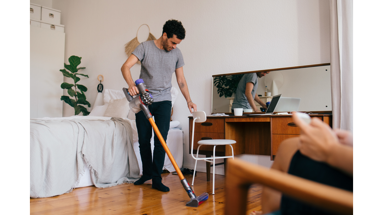 Full length of man cleaning bedroom with vacuum cleaner