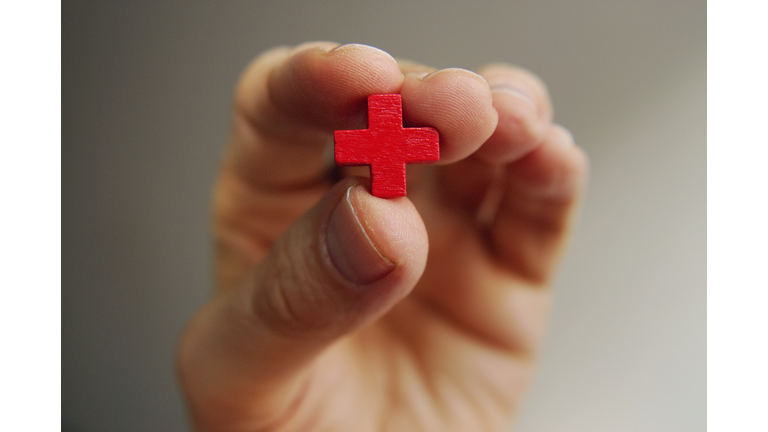 Male fingers hold a little red cross