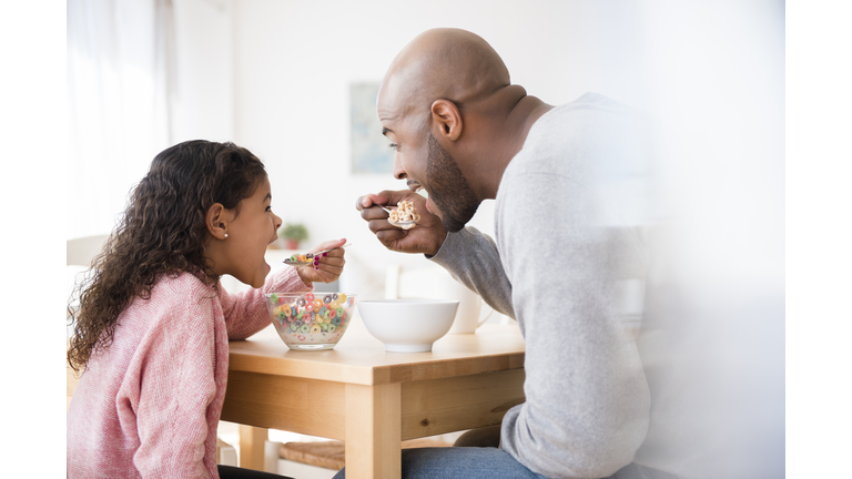 Father and daughter eating cereal at table