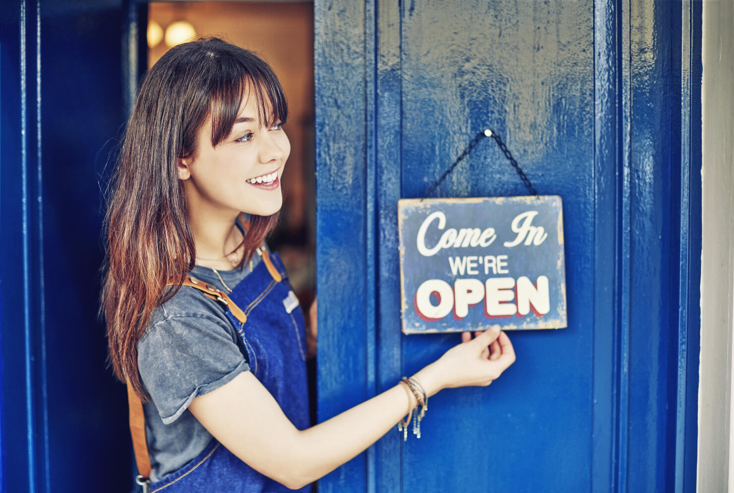 Smiling female entrepreneur hanging open sign on deli door