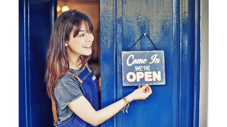 Smiling female entrepreneur hanging open sign on deli door