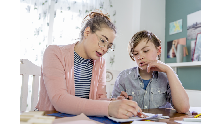 Private tutoring lesson for 10 years old blonde primary school boy while doing his homework together with female tutor in her twenties.