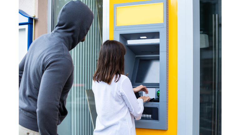 Thief Looking At Woman Entering The Pin In ATM