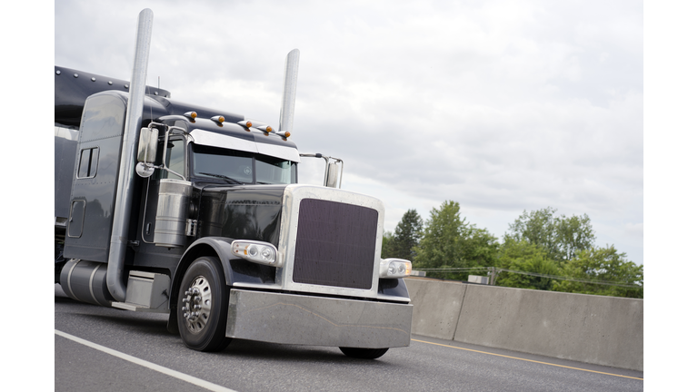 Black stylish classic big rig semi truck running on road