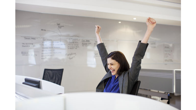 Enthusiastic businesswoman with arms raised in office