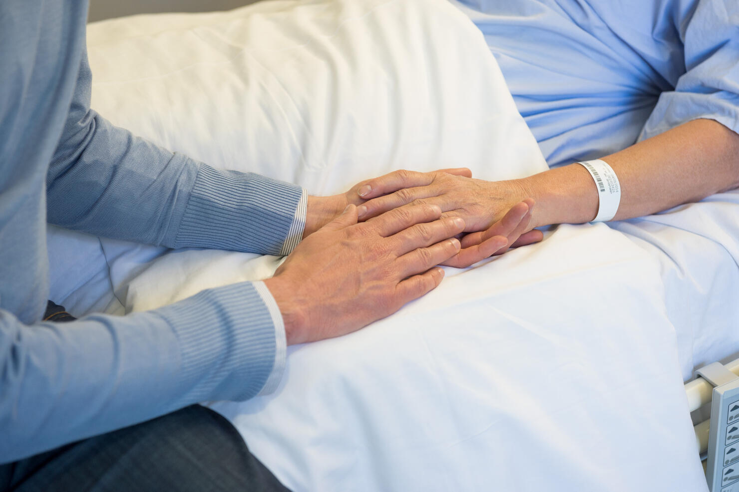 Man holding hands of his mother in hospital bed