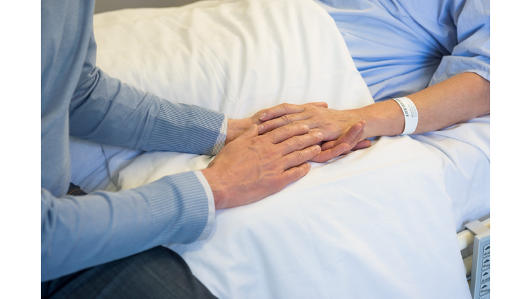 Man holding hands of his mother in hospital bed