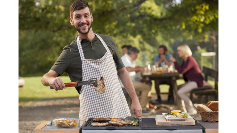 Portrait of man grilling meat at barbecue outdoors
