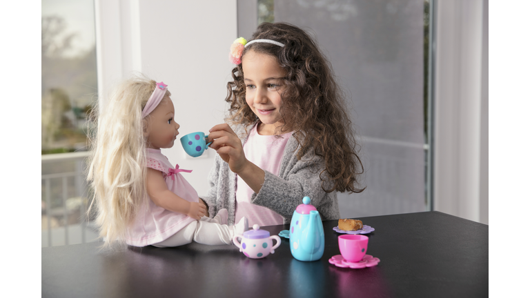 Portrait of smiling little girl playing with doll and doll's china set