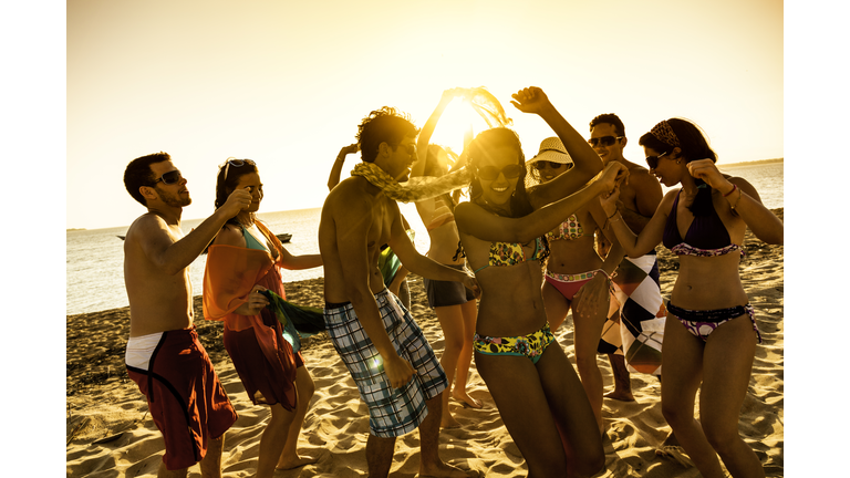 Spring break backlit group of young people dancing on beach