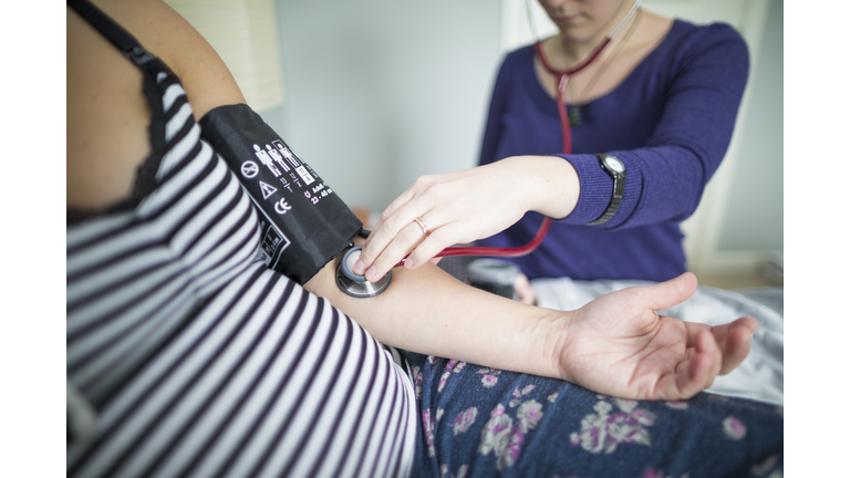 Midsection of midwife examining pregnant woman at home