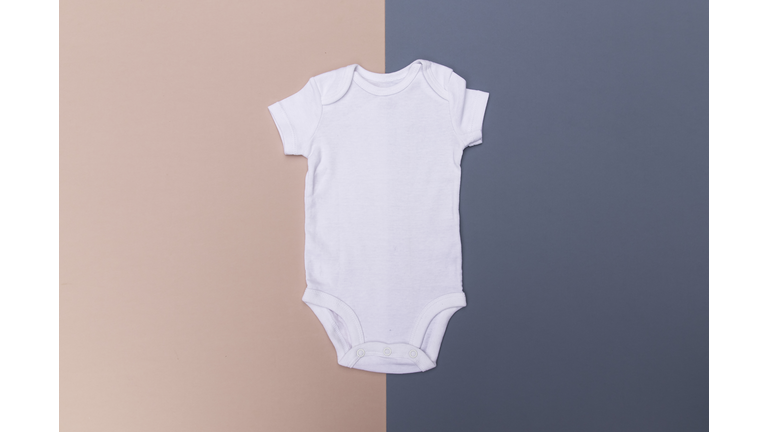 Blank white baby onesie bodysuit on a half and half pink and blue background - gender reveal
