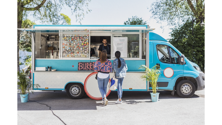 Full length rear view of female friends talking with male food truck owner in city on sunny day