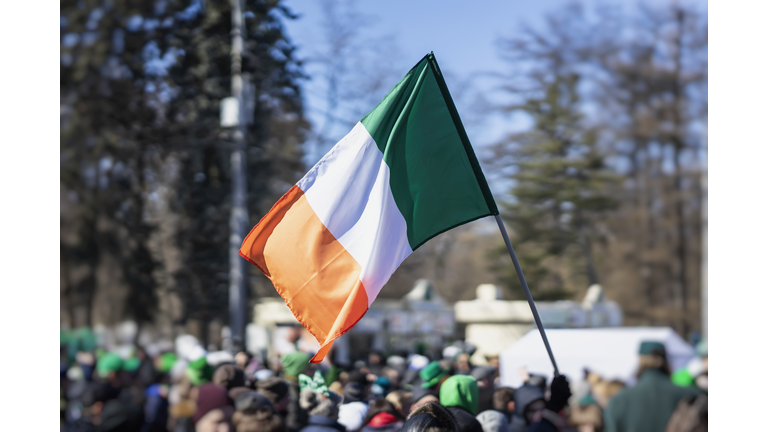 Flag of Ireland close-up in hands on background of blue sky during the celebration of St. Patrick's Day